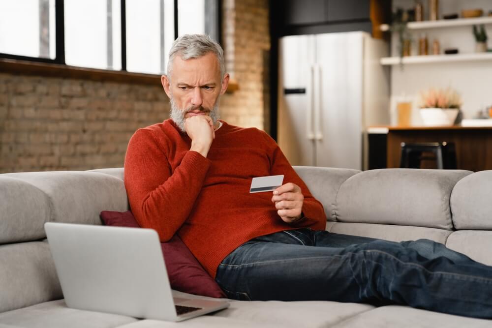 Old man with credit card, looking at his laptop
